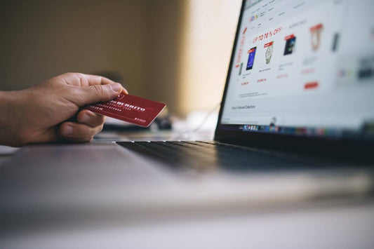 A person holding a credit card while shopping online, looking for the best online deals on a laptop.