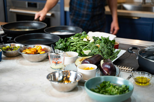 Person preparing vegetables with bowls, pans, and fresh ingredients on a kitchen counter