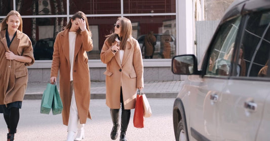 Three women enjoying a shopping day, walking with shopping bags in hand, wearing stylish coats.