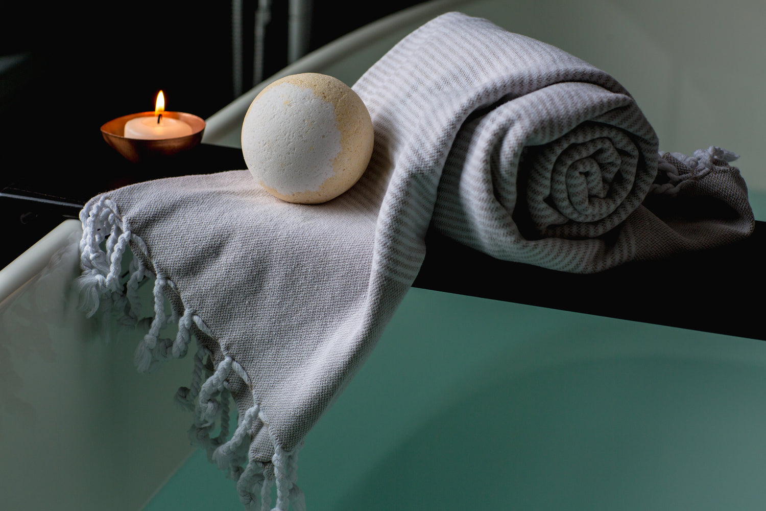 Luxury beauty and personal care essentials featuring a rolled bath towel, bath bomb, and lit candle for a relaxing spa-like experience.