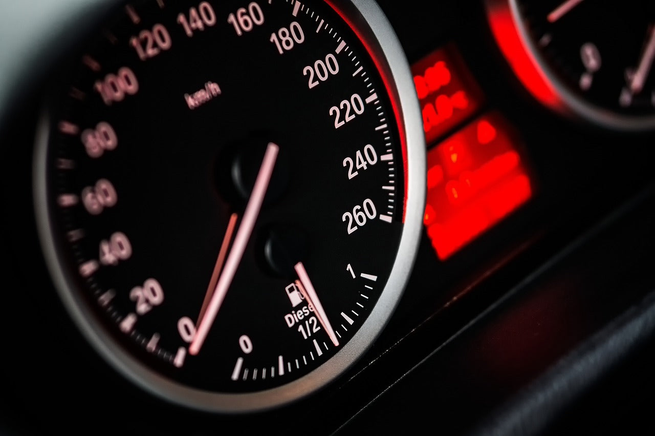 Close-up of a car speedometer on a dashboard with illuminated red and black details, highlighting automotive design and performance accessories.