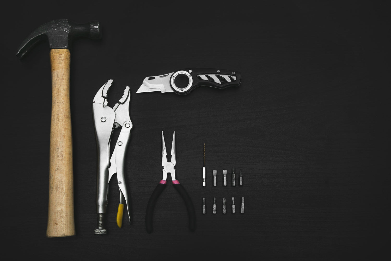 A set of essential tools for home improvement, including a hammer, pliers, utility knife, and drill bits, neatly arranged on a dark surface.