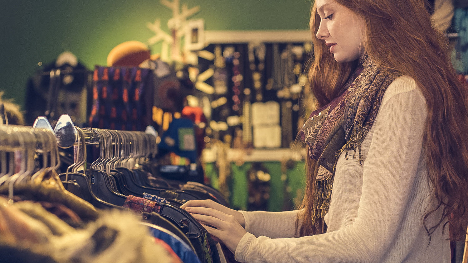 Woman browsing clothing rack with stylish apparel and accessories in a cozy boutique.