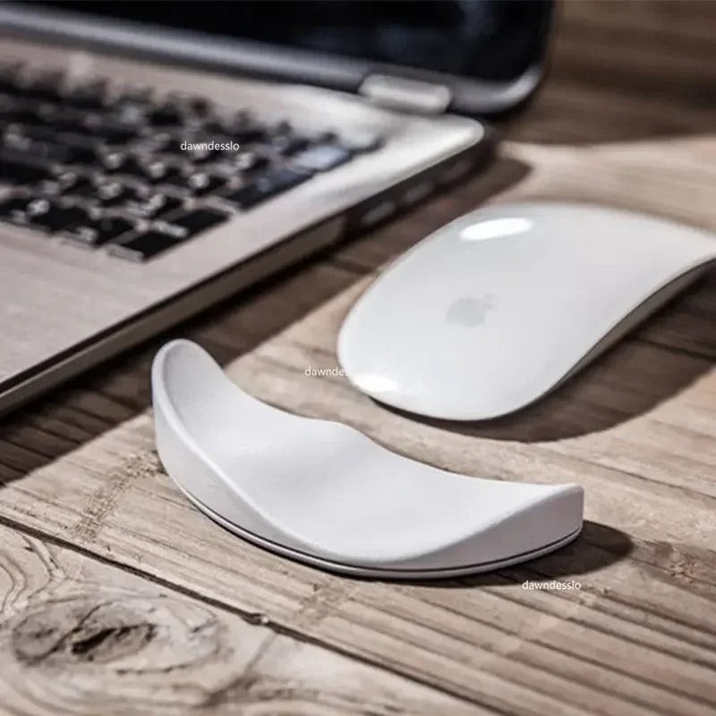 Ergonomic mouse pad wrist support placed next to a laptop and wireless mouse on a wooden desk.