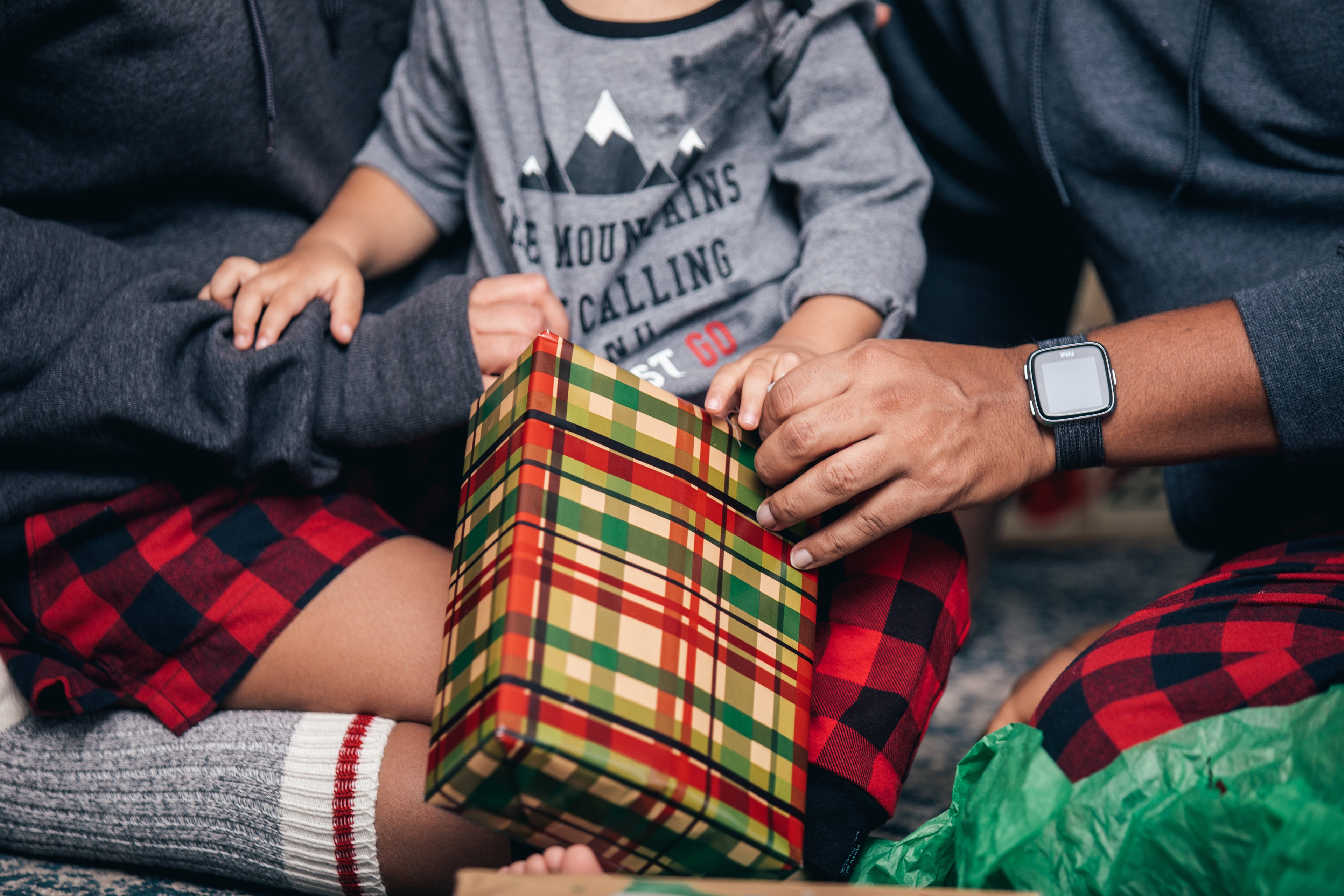 Family sharing a wrapped gift in cozy holiday attire, representing the warmth and joy of shopping at Deal Source Online