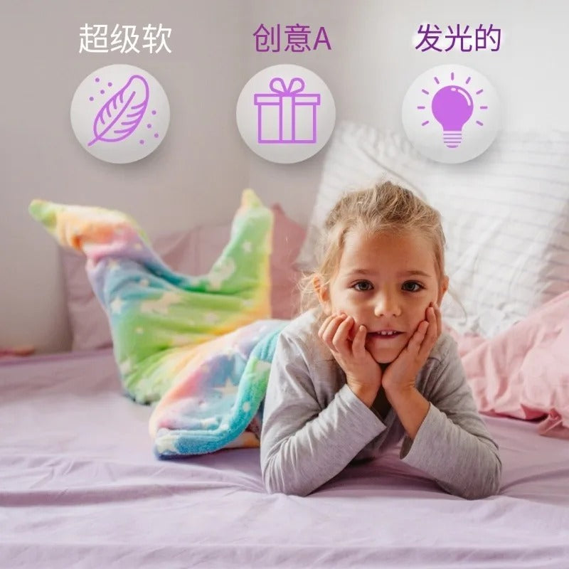Young girl on bed smiling while wearing Mermaid Galaxy Glow Blanket with icons for softness and glow-in-the-dark features