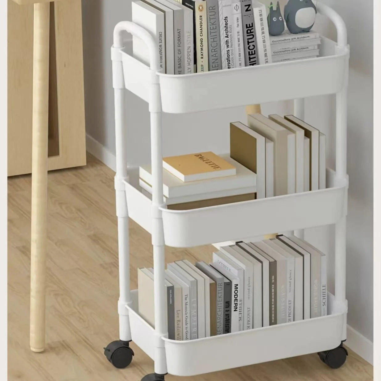 White multi-purpose storage cart with three tiers, holding books in a modern home setting.