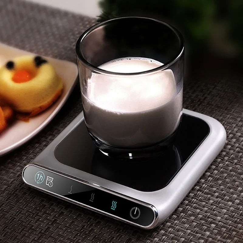 Glass cup of warm milk on a USB-powered heated coaster for drinks.